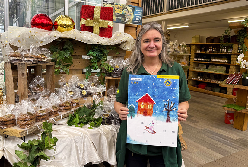 Tropica Mitarbeiterin hält Lions-Kalender im Hintergrund festlich geschmückte Feinkost-Regale