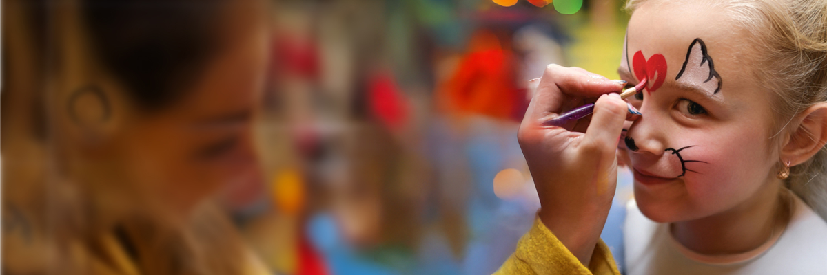 Kind erhält Katzen-Gesichtsbemalung mit rotem Herz auf der Stirn.